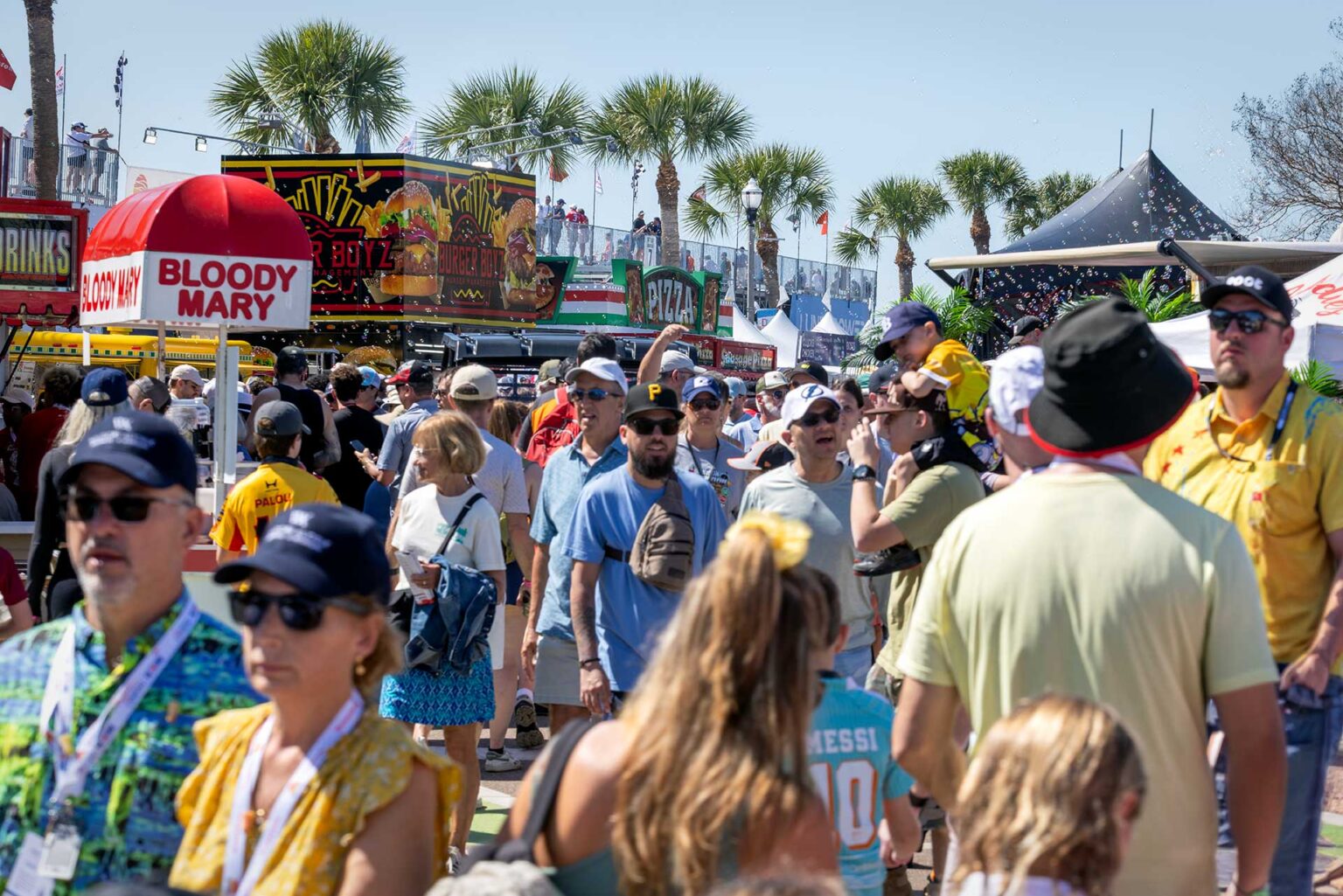 Fans crowding the food and drink midway under palm trees and blue sky