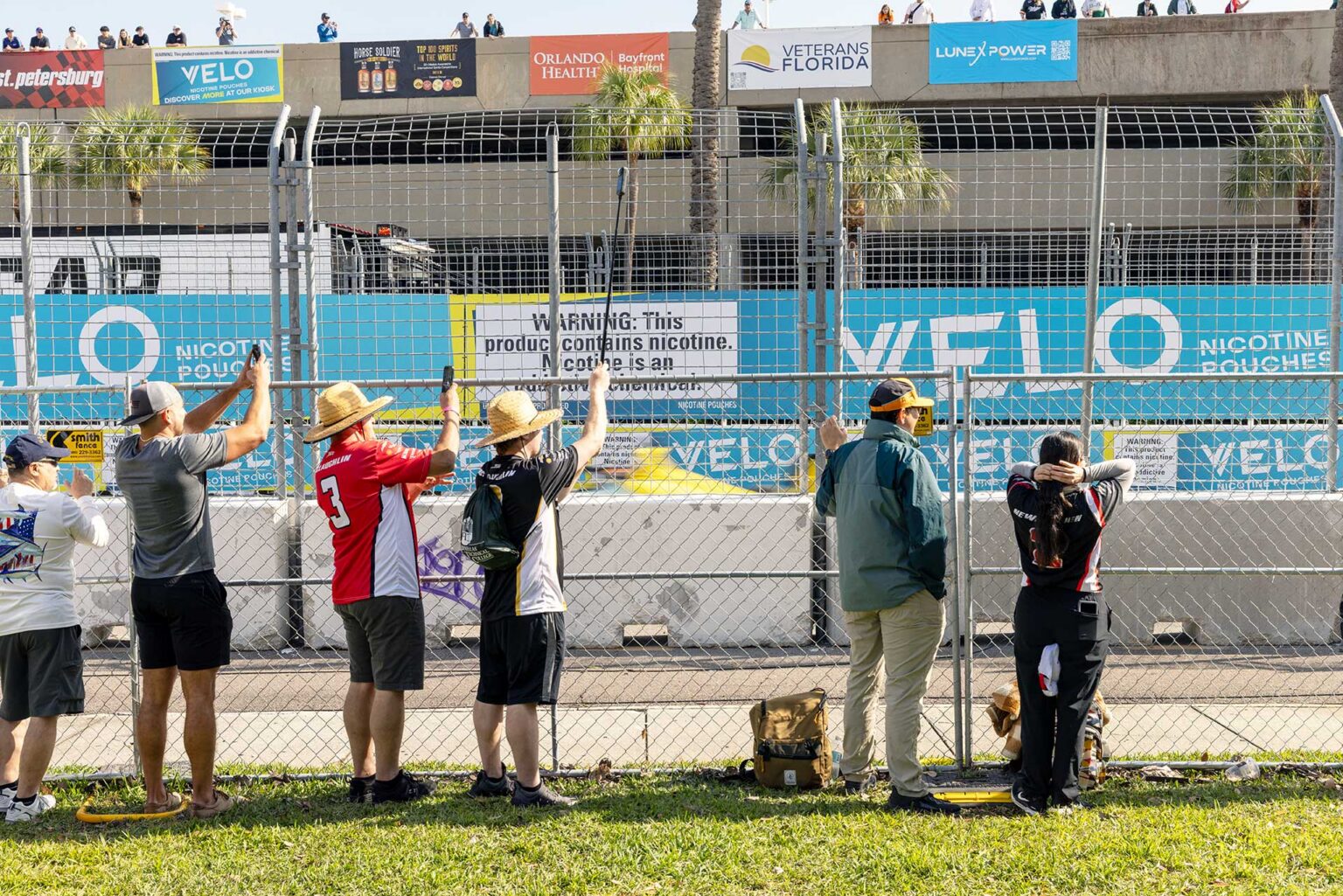 Spectators lined up along the catch fence photographing the cars on track