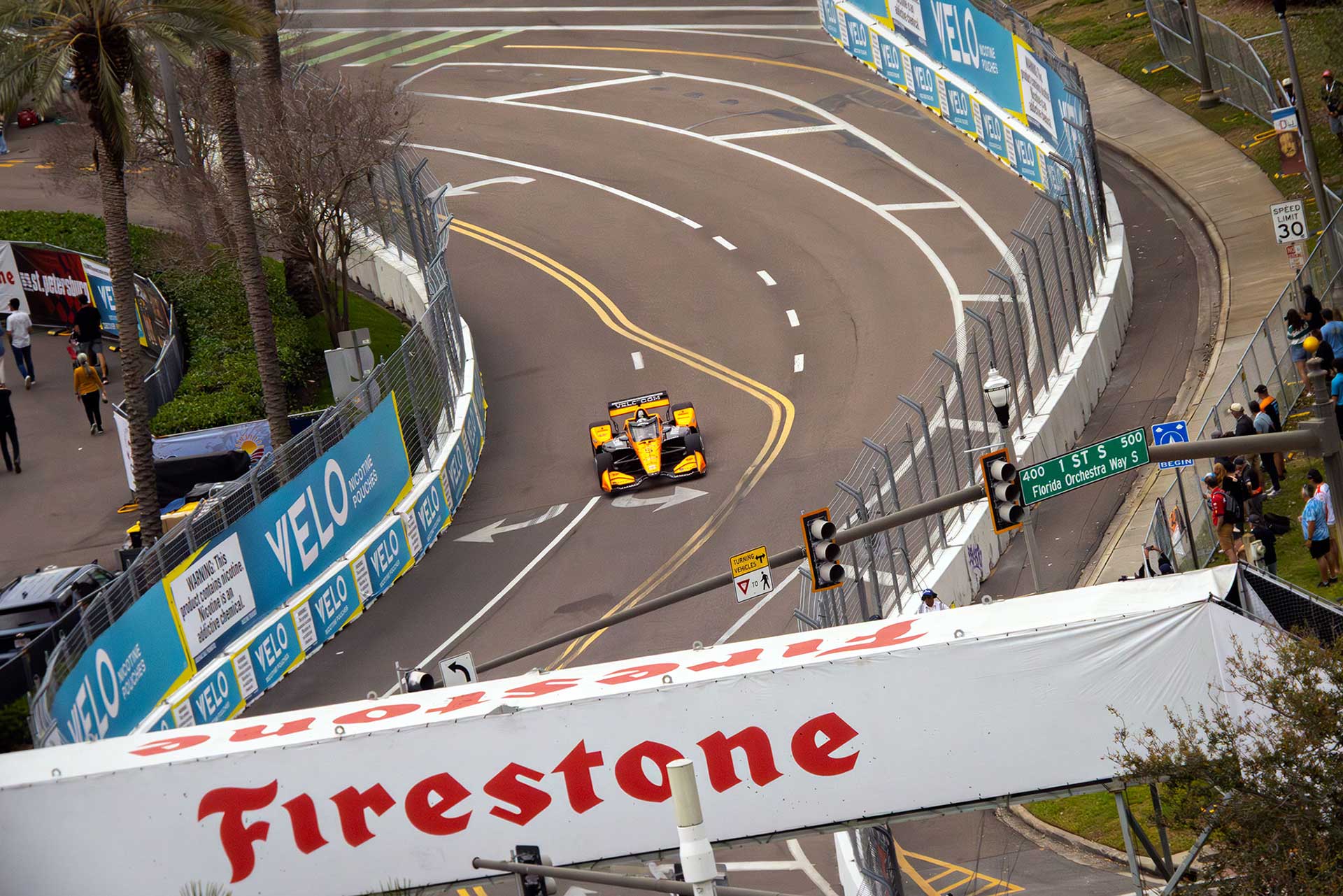 Elevated view of a car threading the downtown S-curve beneath a large Firestone banner
