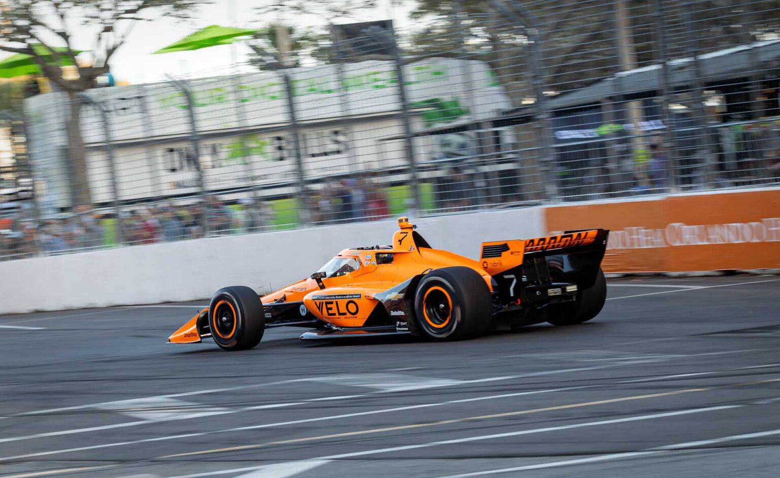A papaya Arrow McLaren car at speed in warm late-afternoon light