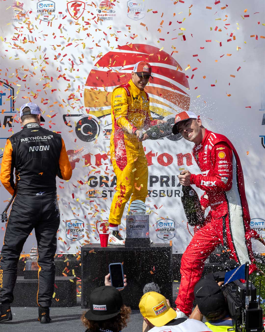 Drivers spraying champagne on the podium in front of the Firestone Grand Prix backdrop